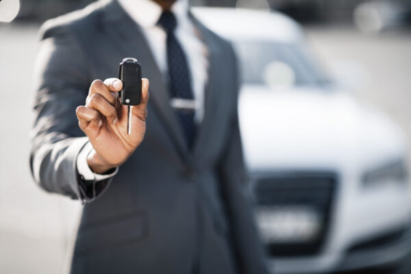 Car sale and rental concept. Businessman showing car key against luxury auto