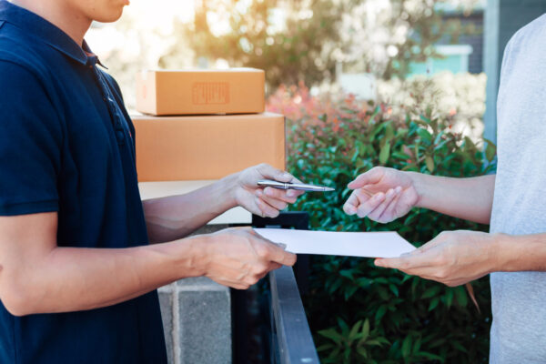 Young asian delivery staff holding the pen and documents submitting giving to the customer receiving the parcel at front house.